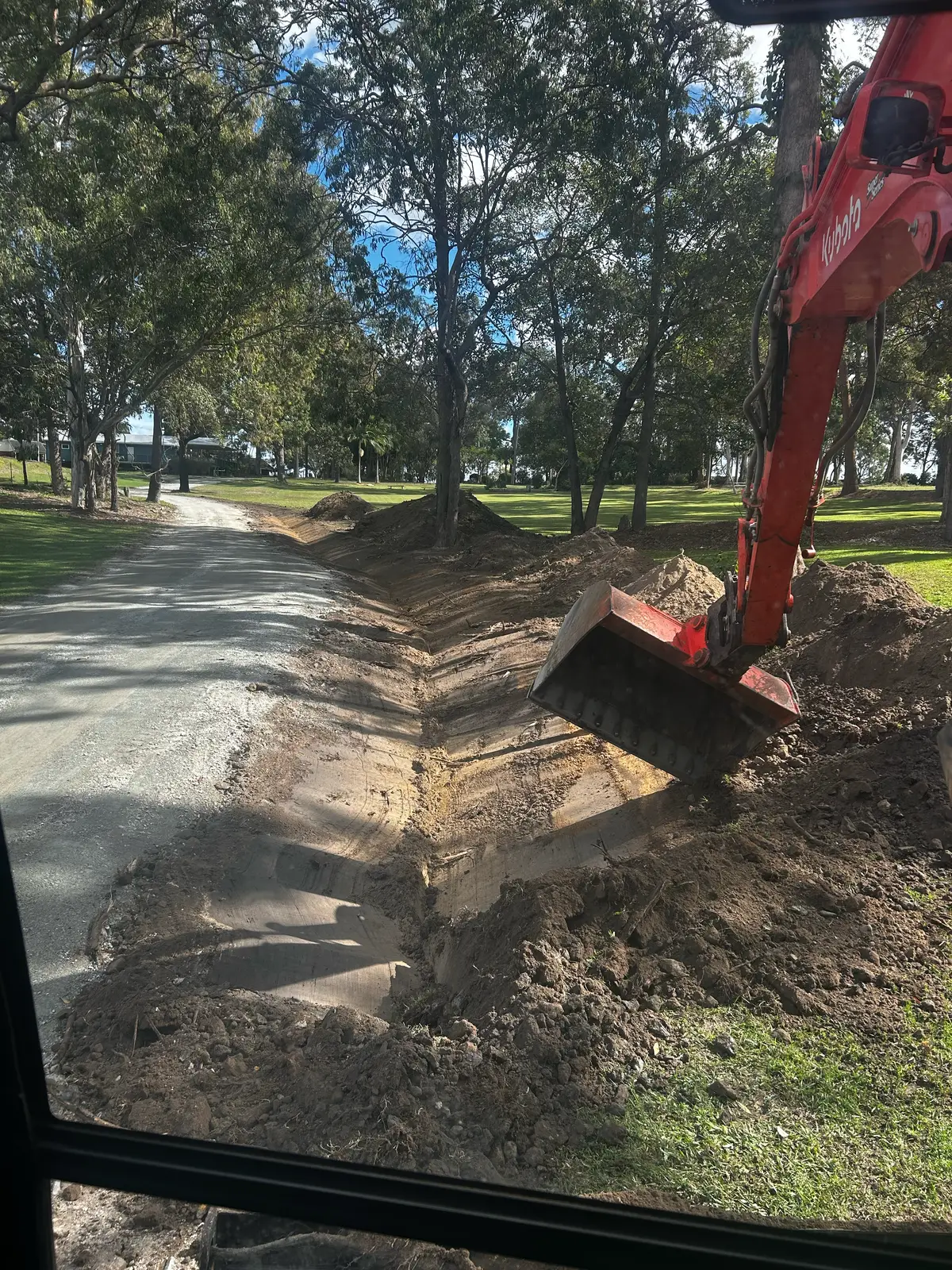 Excavator cutting a drainage swale beside a driveway on a rural property in Queensland